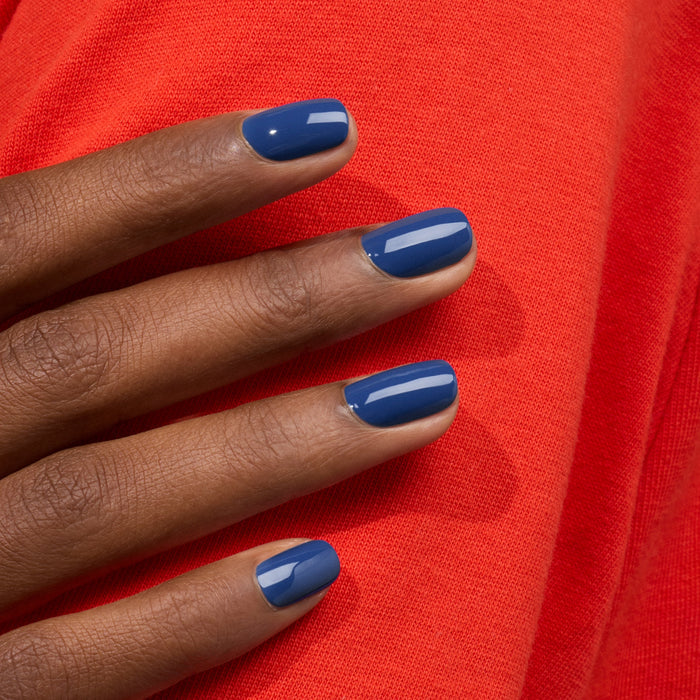 A hand with neatly manicured nails painted in "Midnight" by Manucurist rests on bright red fabric, creating a vivid color contrast.