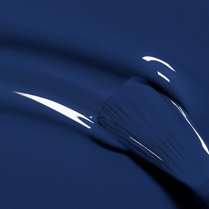 A close-up of a brush spreading Manucurist's Midnight—glossy, deep blue nail polish—with visible strokes and light reflections, capturing its sleek allure.
