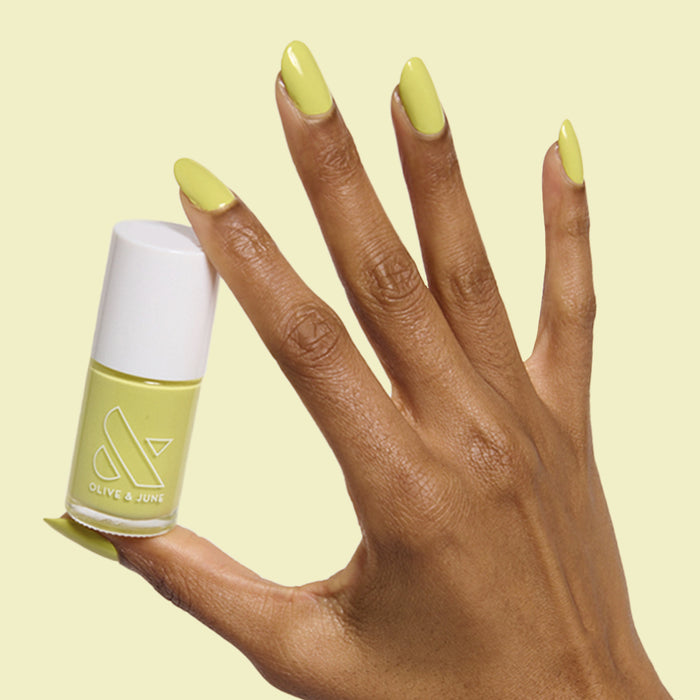 Hand with medium-length oval nails painted chartreuse green in Not Kale gel polish by Olive and June holding polish bottle