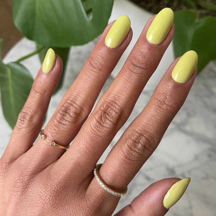 Hand with oval nails painted bright zesty chartreuse gel polish in Not Kale by Olive and June against green leaf background
