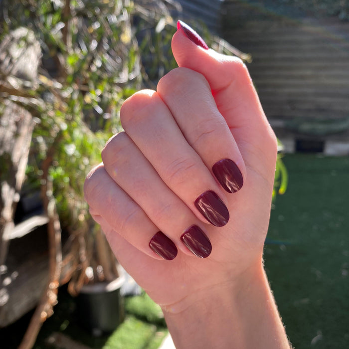 Obsessed - Press-On | Extra Short | Round hand showing glossy dark ruby red false nails in natural light outdoors