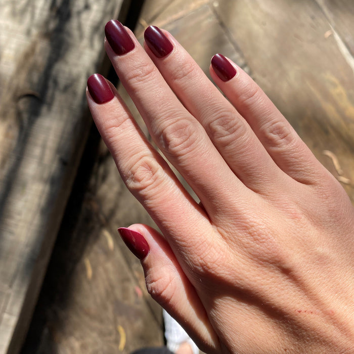 Obsessed - Press-On | Extra Short | Round hand displaying glossy dark ruby red false nails in natural sunlight