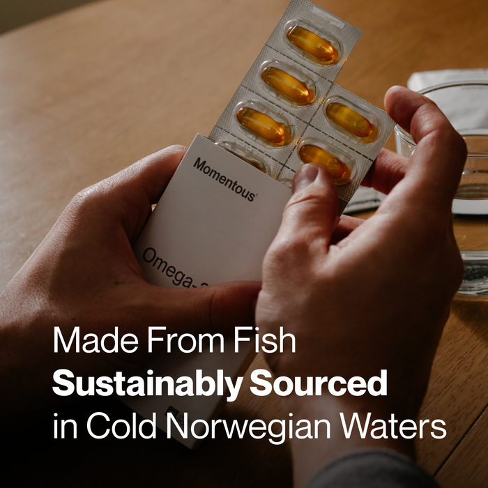 Hand holding white Momentous Omega-3 travel pack with five amber capsules in blister strips.