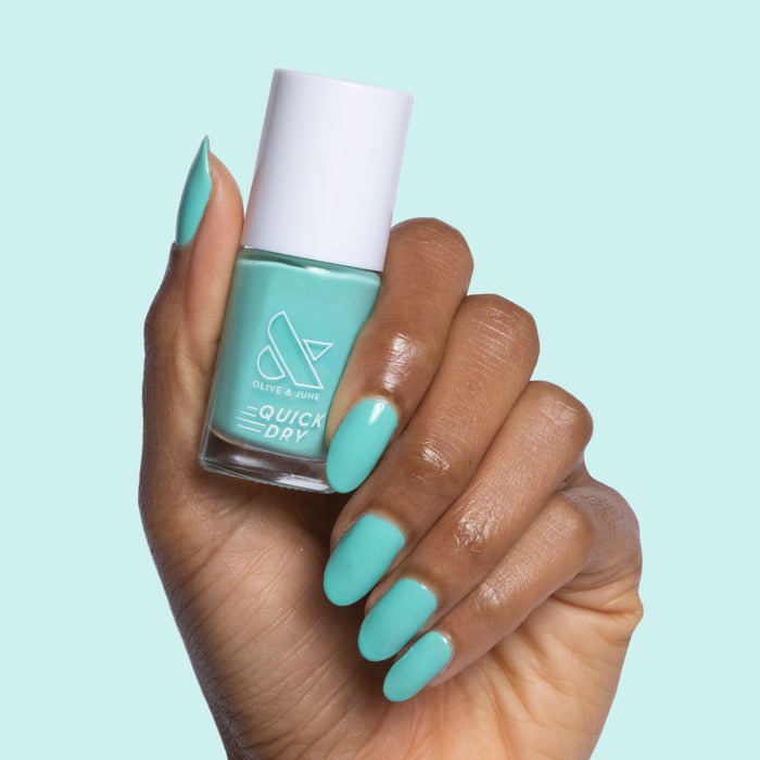 Hand holding Olive and June Parakeet quick dry gel polish with nails painted electric turquoise blue
