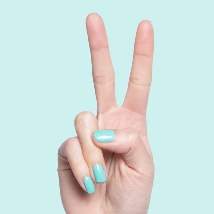 Hand showing peace sign with nails painted in glossy electric turquoise Parakeet gel polish against light blue background