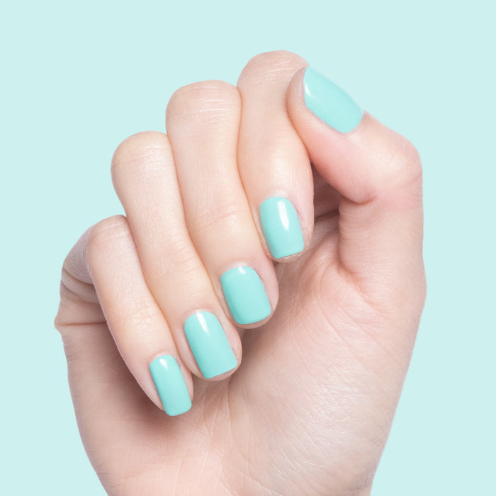 Hand with nails painted in glossy Parakeet quick dry gel polish against a light turquoise background