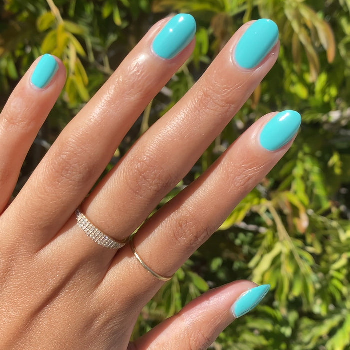 Hand with nails coated in glossy Parakeet gel polish in sunlight with green leaves background