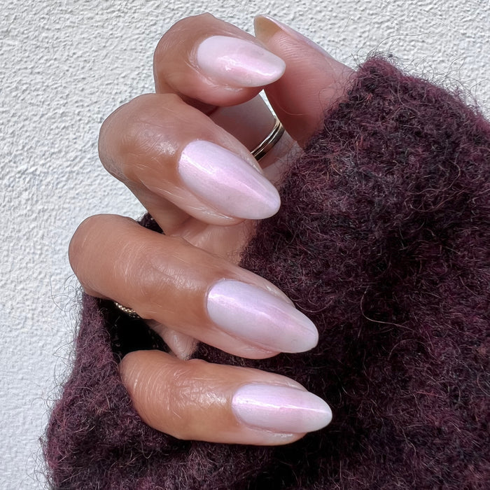 Hand featuring almond-shaped nails painted with Pink Capiz long-lasting polish in soft iridescent pink shade