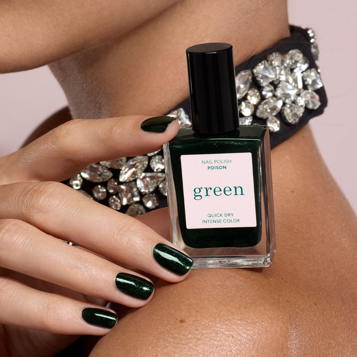 A person with neatly manicured nails painted in Poison by Manucurist holds a matching Poison nail polish bottle. They wear a jeweled choker, and the background is neutral.