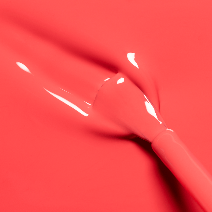 A close-up of a brush stroke in Manucurist's Pulp, a glossy, bright grapefruit nail polish, with the brush partially visible and wet streaks highlighting its vibrant texture.