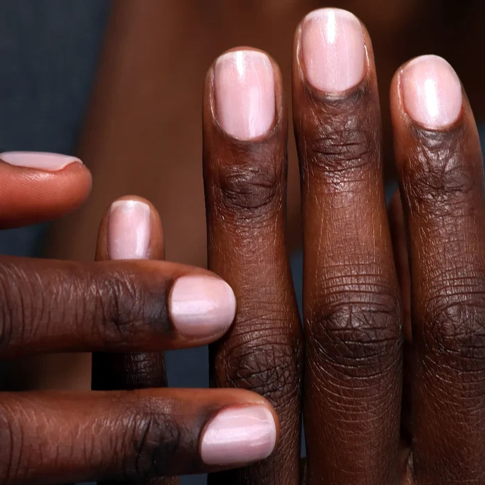 Close-up of two hands with short, neatly manicured nails painted an ethereal light pink using LONDONTOWN Quartz Illuminating Nail Concealer.