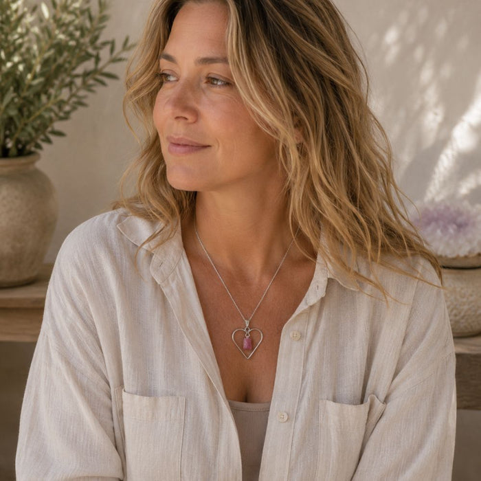 Woman wearing a raw pink tourmaline heart pendant on a silver chain with a neutral linen top, photographed in natural daylight.