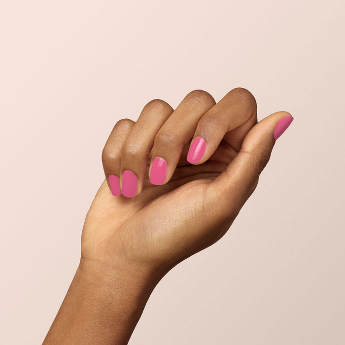 A hand with medium brown skin is shown against a pale background, fingers gently curled to display neatly manicured nails painted with Manucurist’s Green™ nail polish in the shade Rose.