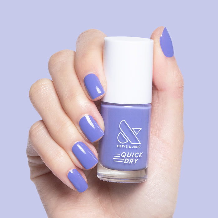 Hand holding Olive and June Royal quick dry polish bottle with deep purple gel polish on manicured nails