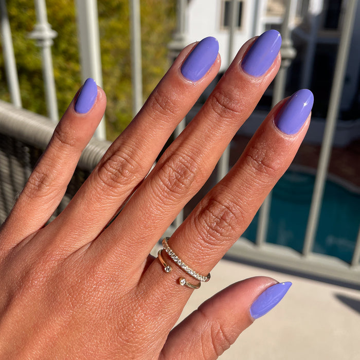 Hand with Royal quick dry gel polish in glossy regal purple on natural nails by a bright outdoor pool setting