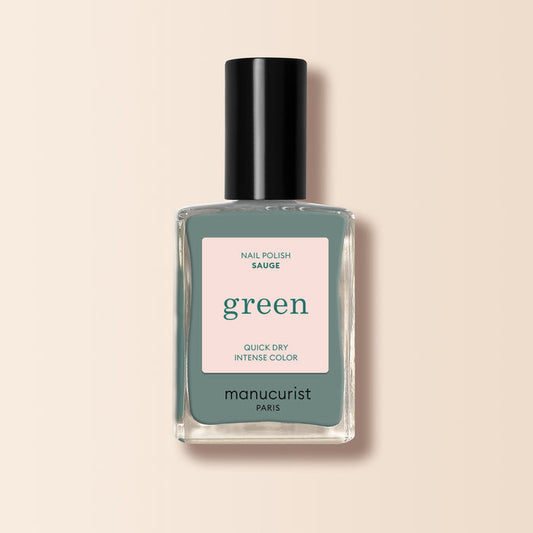 A bottle of Manucurist nail polish in the shade Sage, with a black cap and a label reading "green, quick dry intense color," is shown against a light beige background.