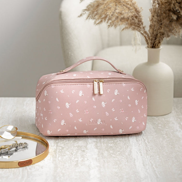 Pink floral-patterned cosmetic bag on a table with a vase and jewelry in the background