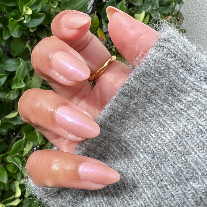 Hand with almond-shaped nails polished in milky golden iridescent Sandy Scallop gel polish wearing a gold ring and gray sweater
