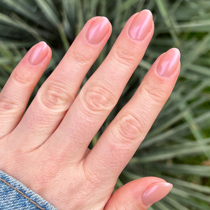 Hand with natural nails painted in glossy Sandy Scallop gel polish showing a soft golden neutral manicure