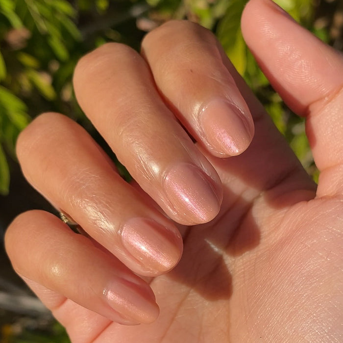 Hand with softly rounded nails painted in Sandy Scallop gel polish showing a milky golden iridescent mani