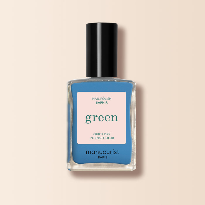 A bottle of Manucurist Saphir nail polish with a striking sapphire blue shade, a black cap, and a beige label featuring green and blue text.