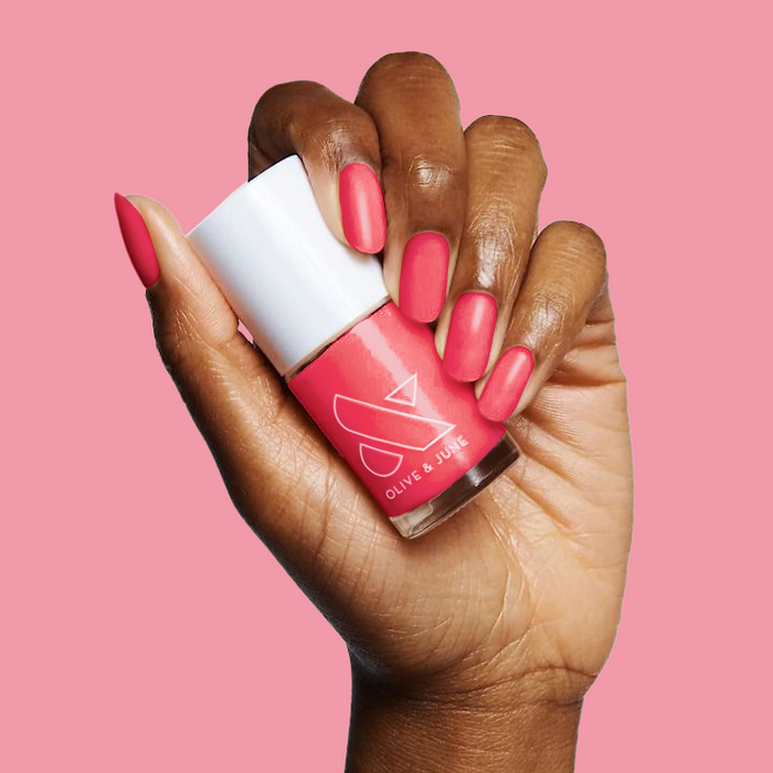 Hand with medium-length nails painted bright jelly pink holding Strawberries Are in Season Right Now gel polish bottle