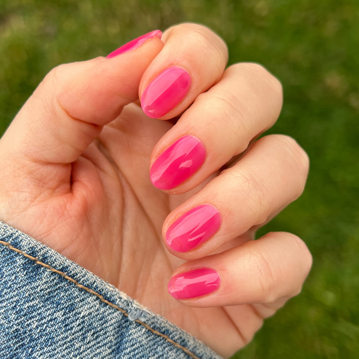 Hand with short nails painted glossy jelly pink in Strawberries Are in Season Right Now manicure by Olive and June