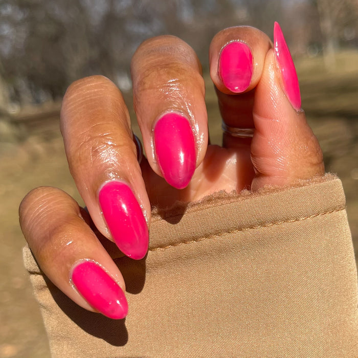 Hand with medium nails painted glossy jelly sheer crimson pink in Strawberries Are in Season Right Now gel polish outdoors