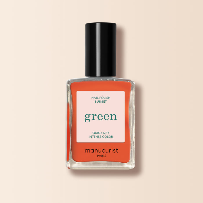 A bottle of Manucurist Sunset nail polish from the Green™ collection, in vibrant orange, with a black cap and white-coral label, displayed on a beige background.