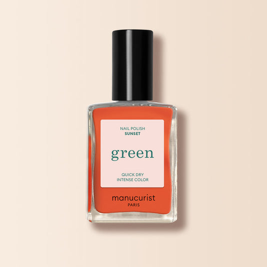 A bottle of Manucurist Sunset nail polish from the Green™ collection, in vibrant orange, with a black cap and white-coral label, displayed on a beige background.