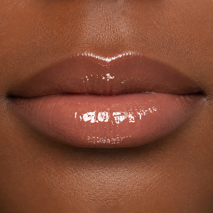 close-up lip image of a woman with a medium-dark skin tone wearing Runway Rogue Classic Lip Gloss in the shade Supermodel, a sheer glossy nude with a lot of shine