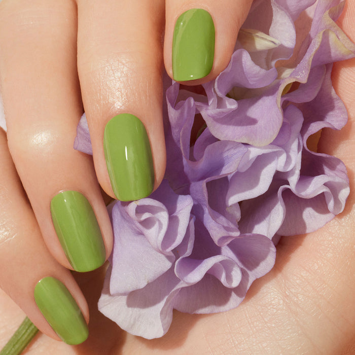 A hand with neatly manicured nails, painted in Manucurist’s Sweet Pea polish, gently holds a soft, pale purple flower.